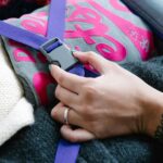 Zbliżenie dłoni zapinającej niebieski pasek na złożone ubrania w walizce, zapewniającej bezpieczne pakowanie.