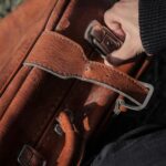 Szczegółowy obraz dłoni trzymającej brązową skórzaną walizkę na zewnątrz, pokazujący fakturę i wzór.