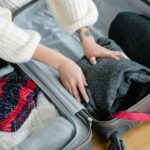 Zbliżenie na dłonie pakujące przytulne swetry i dzianiny do walizki na wycieczkę.