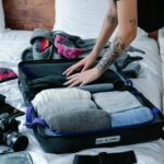 Wytatuowany dorosły organizuje ubrania w walizce, przygotowując się do podróży w pomieszczeniu.