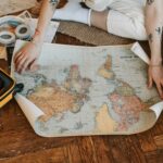 Podróżnik planuje podróż, siedząc na podłodze z mapą świata i walizką wypełnioną najpotrzebniejszymi rzeczami.