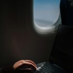 Osoba korzystająca z laptopa podczas lotu i wykazująca produktywne nawyki związane z podróżowaniem.