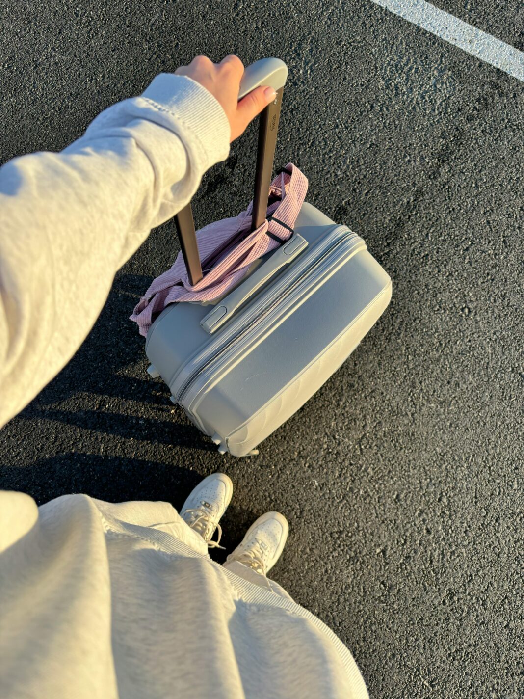 Osoba trzymająca walizkę na kółkach w słoneczny dzień, gotowa do podróży.