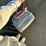 Osoba trzymająca walizkę na kółkach w słoneczny dzień, gotowa do podróży.