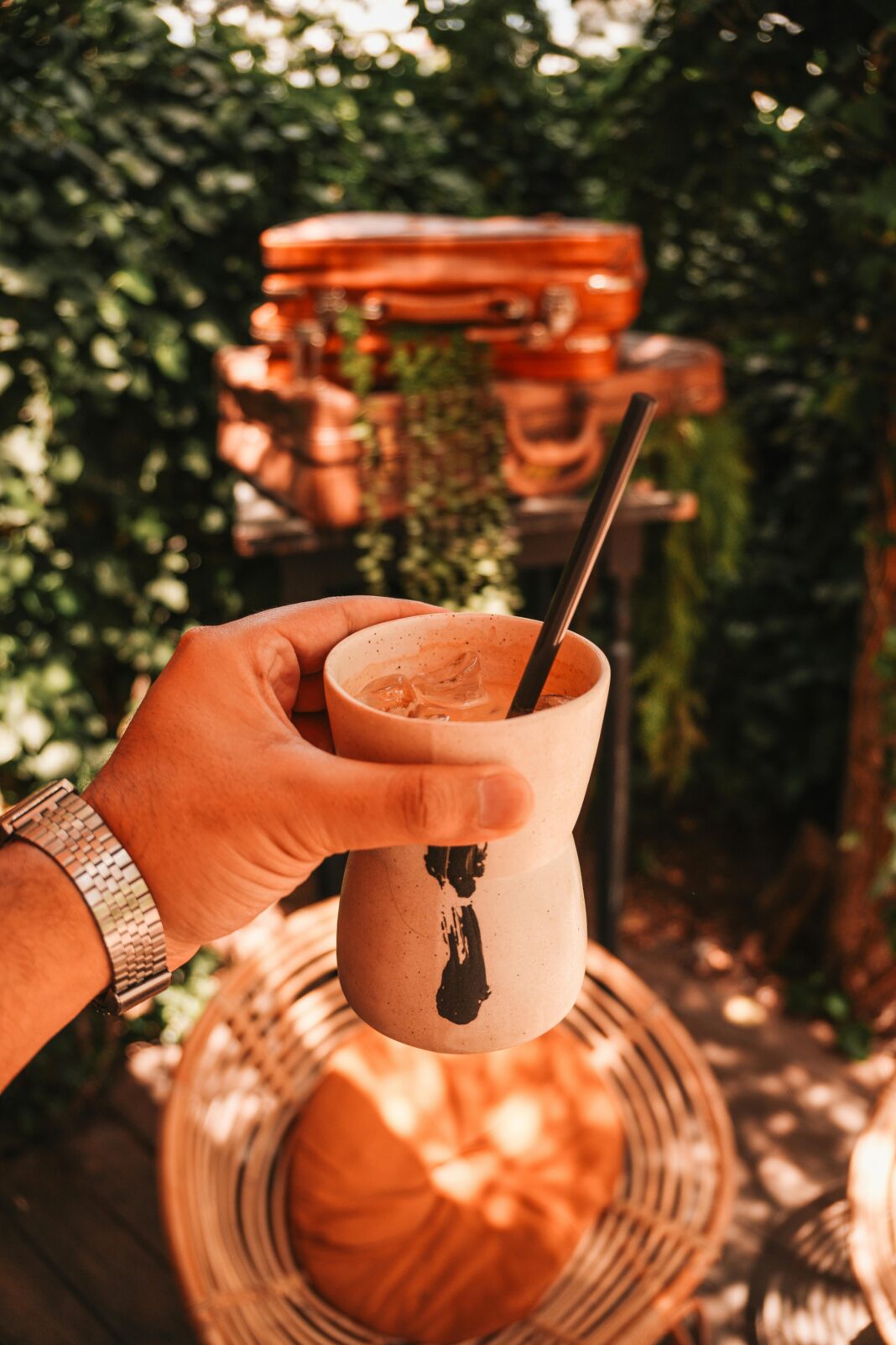 Osoba pijąca kawę w stylowej przestrzeni na świeżym powietrzu z bagażem i zielenią.