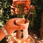 Osoba pijąca kawę w stylowej przestrzeni na świeżym powietrzu z bagażem i zielenią.