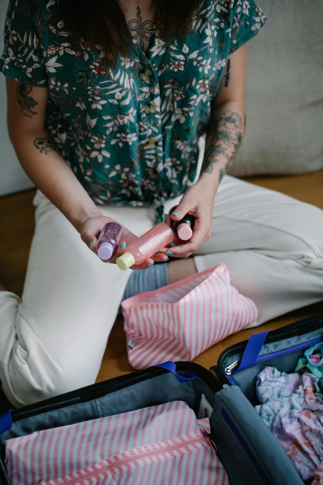 Osoba organizująca przybory toaletowe w walizce na wyjazd, zawierająca butelki podróżne i saszetkę w paski.