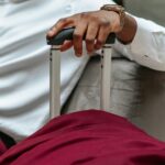 Zbliżenie dłoni podróżującego w interesach spoczywającej na rączce walizki, ubranej w swobodny strój.