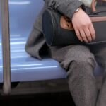 Bagaż podręczny dla rodziny – jak spakować się efektywnie? Przytnij nierozpoznawalną kobietę w modnym płaszczu i spodniach, siedzącą na siedzeniu w pociągu i trzymającą torbę