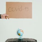 Dłoń trzymająca znak covid-19 nad kulą ziemską i bagażem, symbolizujący wpływ pandemii na podróże.