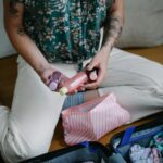 Osoba organizująca przybory toaletowe w walizce na wyjazd, zawierająca butelki podróżne i saszetkę w paski.