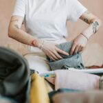 Kobieta z tatuażami pakująca ubrania do walizki na podróż.
