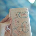 Zbliżenie dłoni trzymającej otwarty paszport z różnymi znaczkami, podkreślające doświadczenia z podróży.