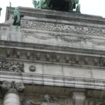 Zbliżenie na łuk Cinquantenaire w Brukseli przedstawiający misterne rzeźby i rzeźby w kamieniu.