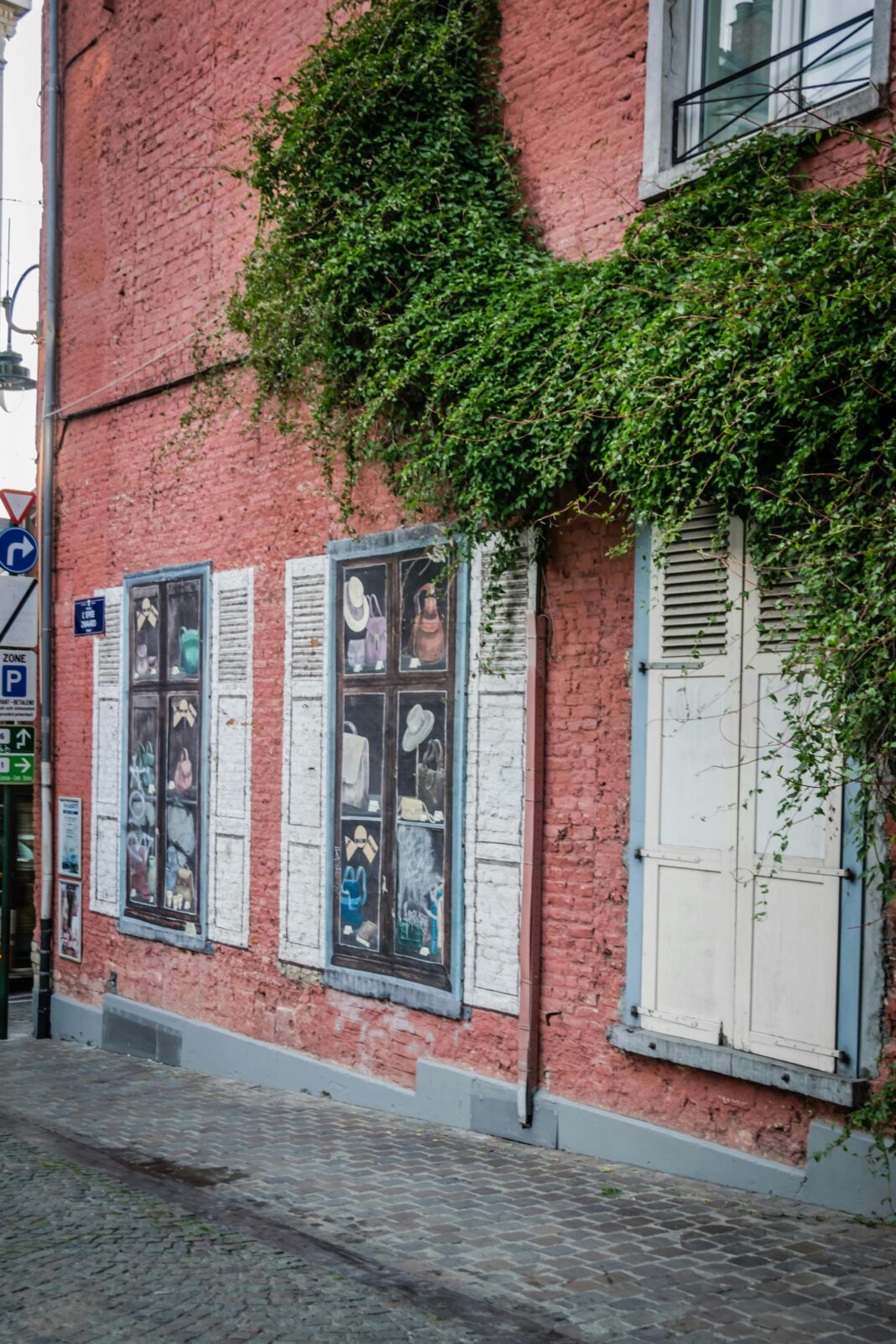 Mur ceglany z bluszczem i artystycznym wystrojem okien na ulicy w Brukseli.