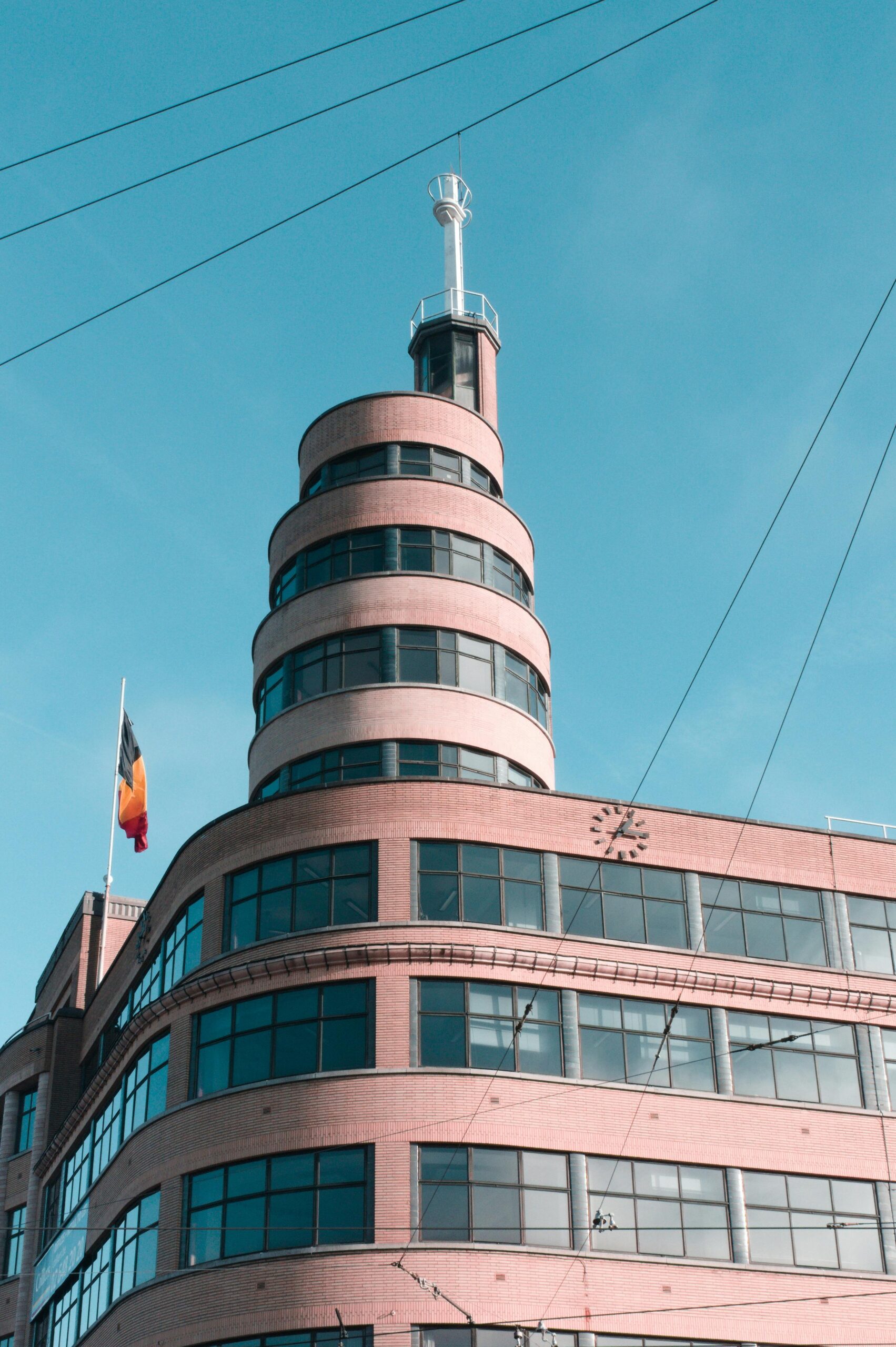 Widok na unikalny spiralny budynek z zegarem i flagą pod czystym, błękitnym niebem.
