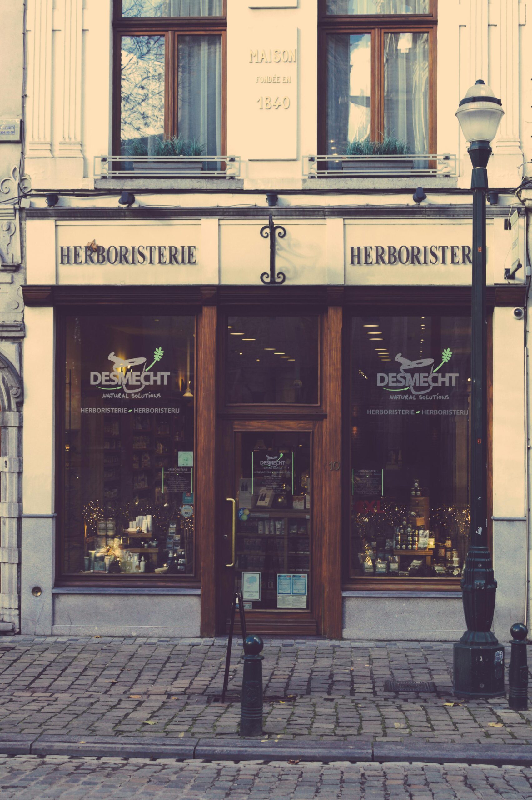 Witryna zabytkowego sklepu z ziołami w europejskim mieście, prezentująca tradycyjny design i brukowaną ścieżkę.
