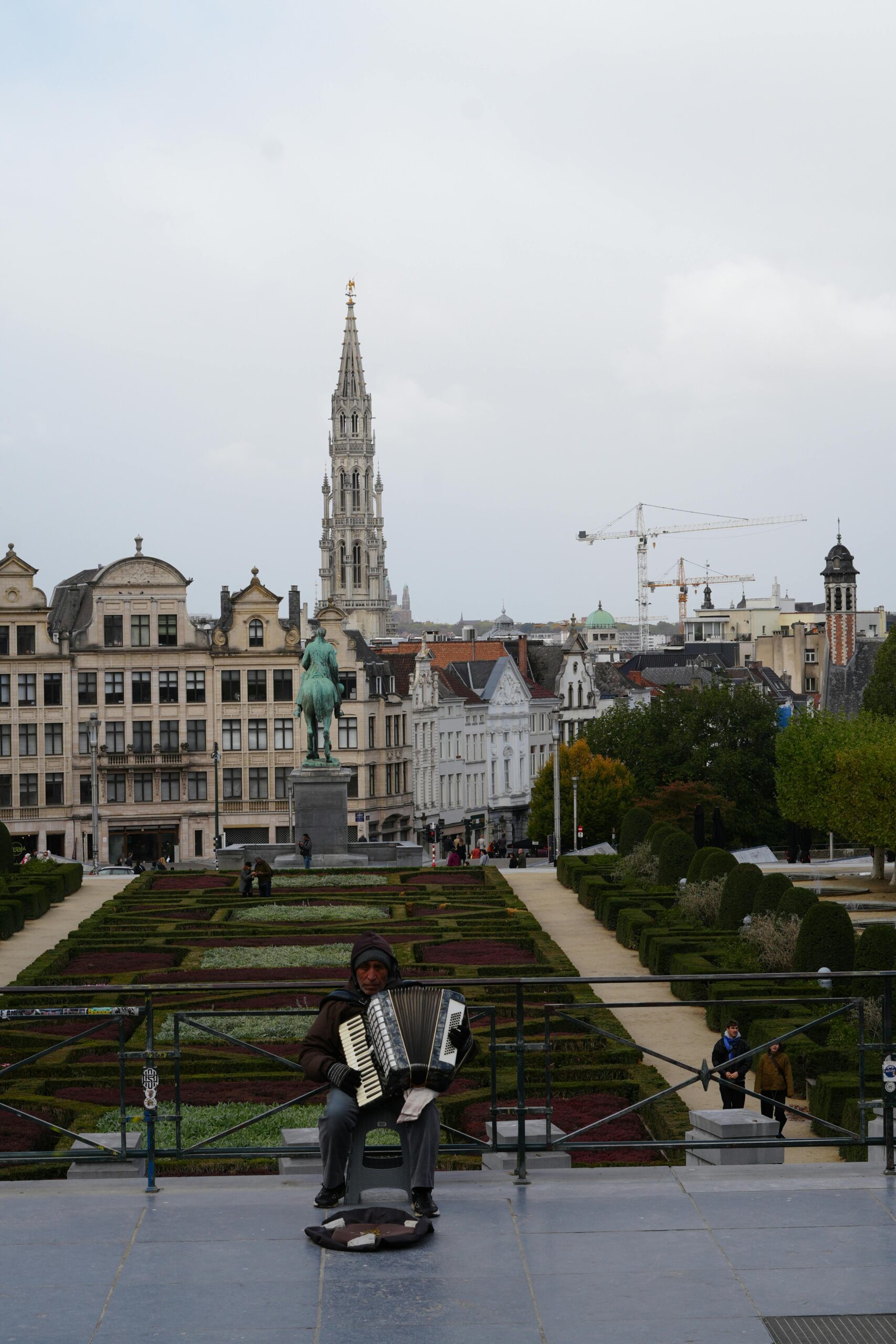 Artysta uliczny grający na akordeonie w Mont des Arts z widokiem na panoramę Brukseli.
