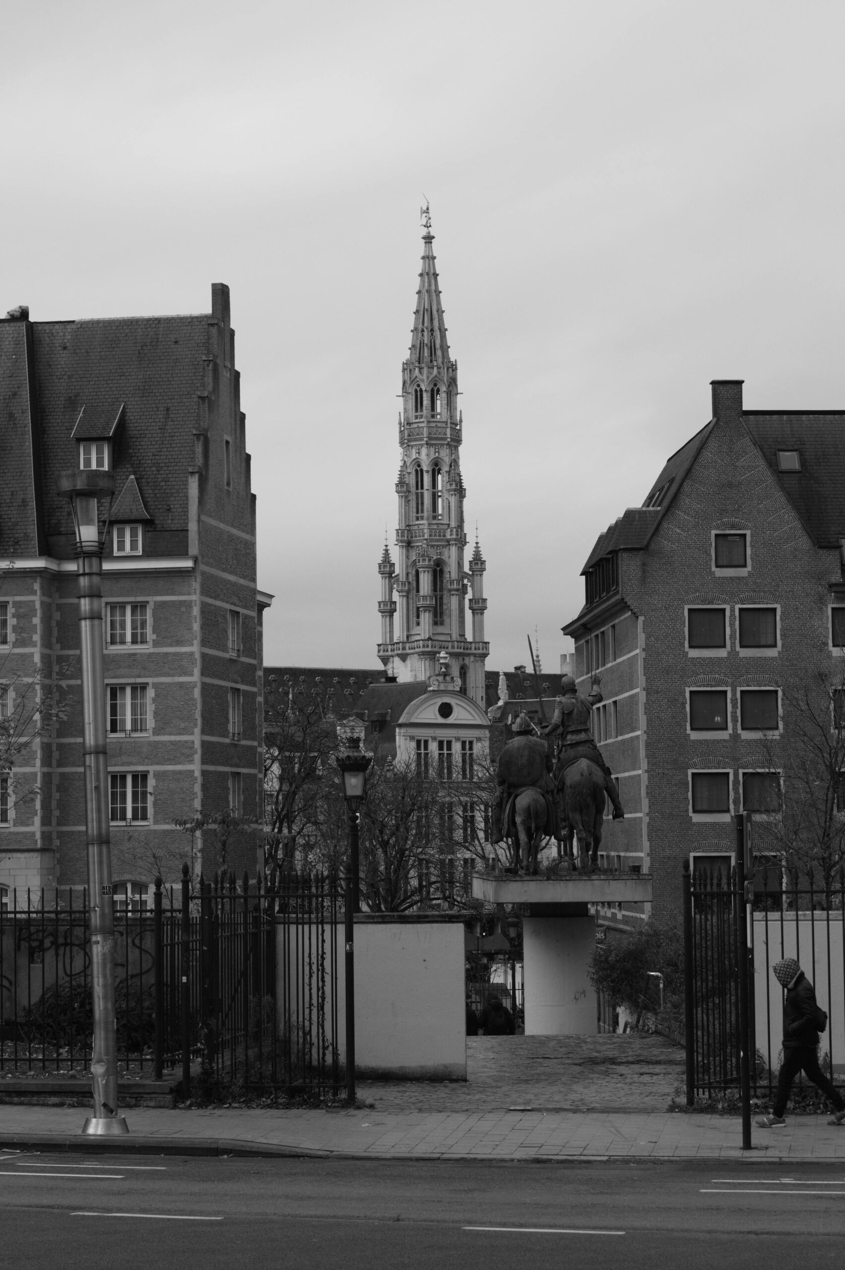 Dramatyczny czarno-biały widok na wieżę ratusza w Brukseli pomiędzy zabytkowymi budynkami.