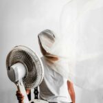 Kreatywny portret przedstawiający osobę z wentylatorem i powiewającą tkaniną w pomieszczeniu.