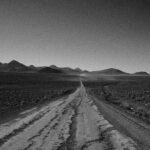 Czarno-białe zdjęcie jałowej, gruntowej drogi prowadzącej przez dystrykt Bolívar, odsłaniającej odległe góry.