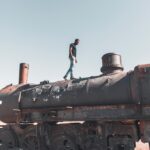 La Paz: Miasto na dachu świata i jego ukryte skarby Mężczyzna spacerujący rustykalną lokomotywą na cmentarzu kolejowym Uyuni w Boliwii pod czystym, błękitnym niebem.