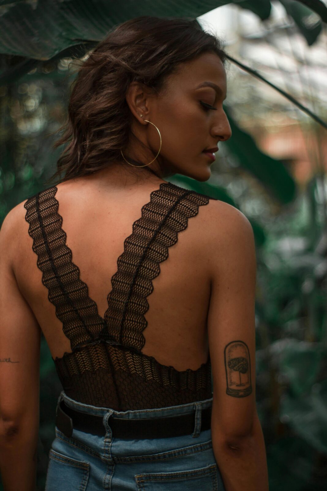 Portret stylowej kobiety z tatuażem w bujnej scenerii na świeżym powietrzu.