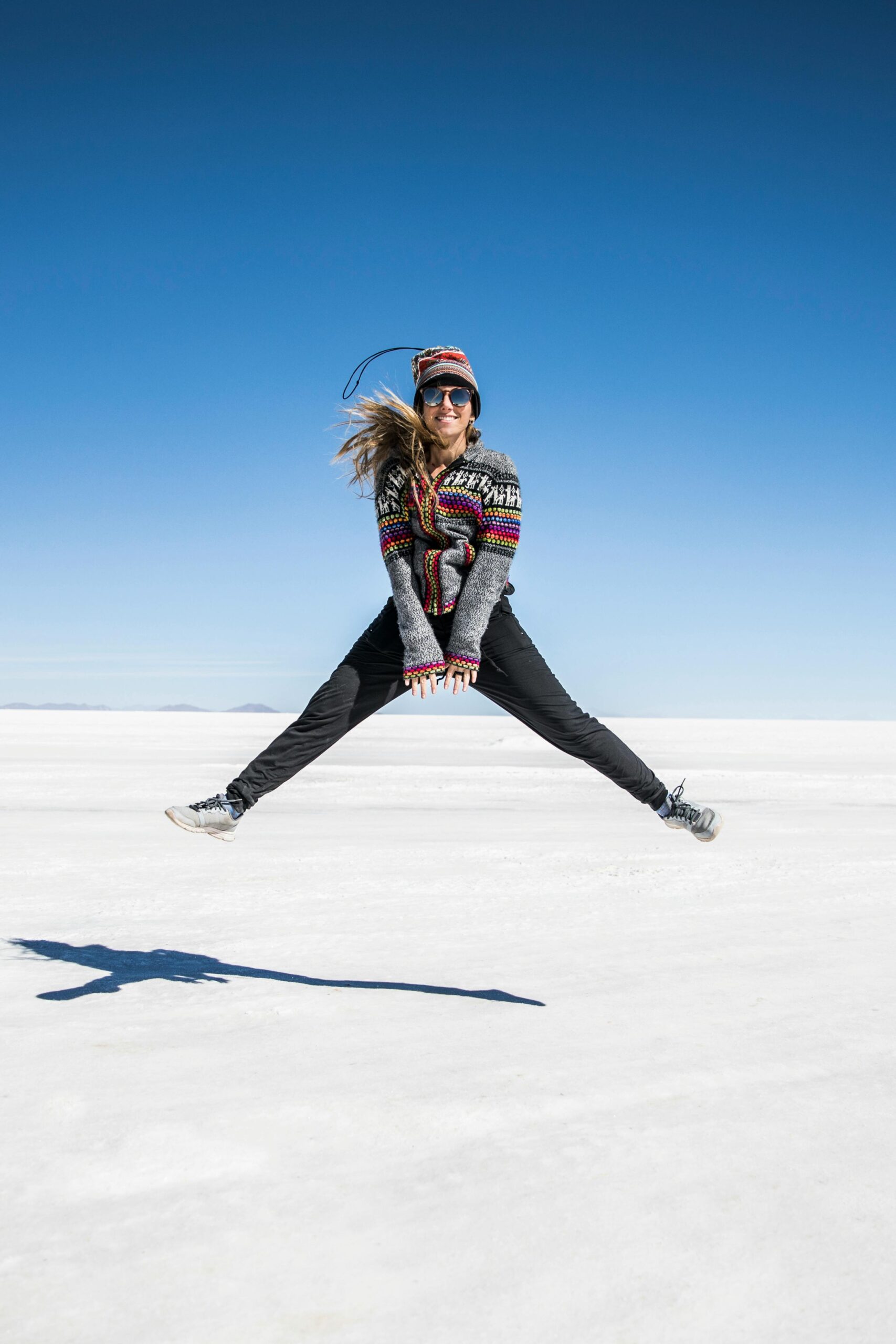 Kobieta skacząca radośnie na rozległym białym obszarze Salar de Uyuni w Boliwii.