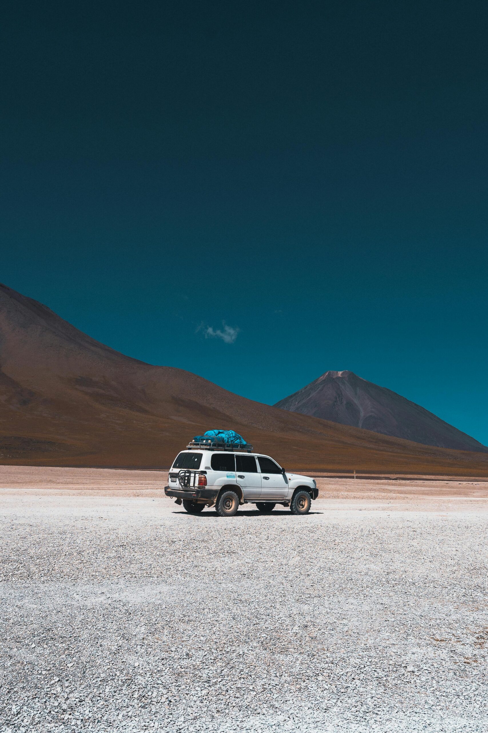 SUV podróżuje przez rozległy pustynny krajobraz Uyuni w Boliwii.