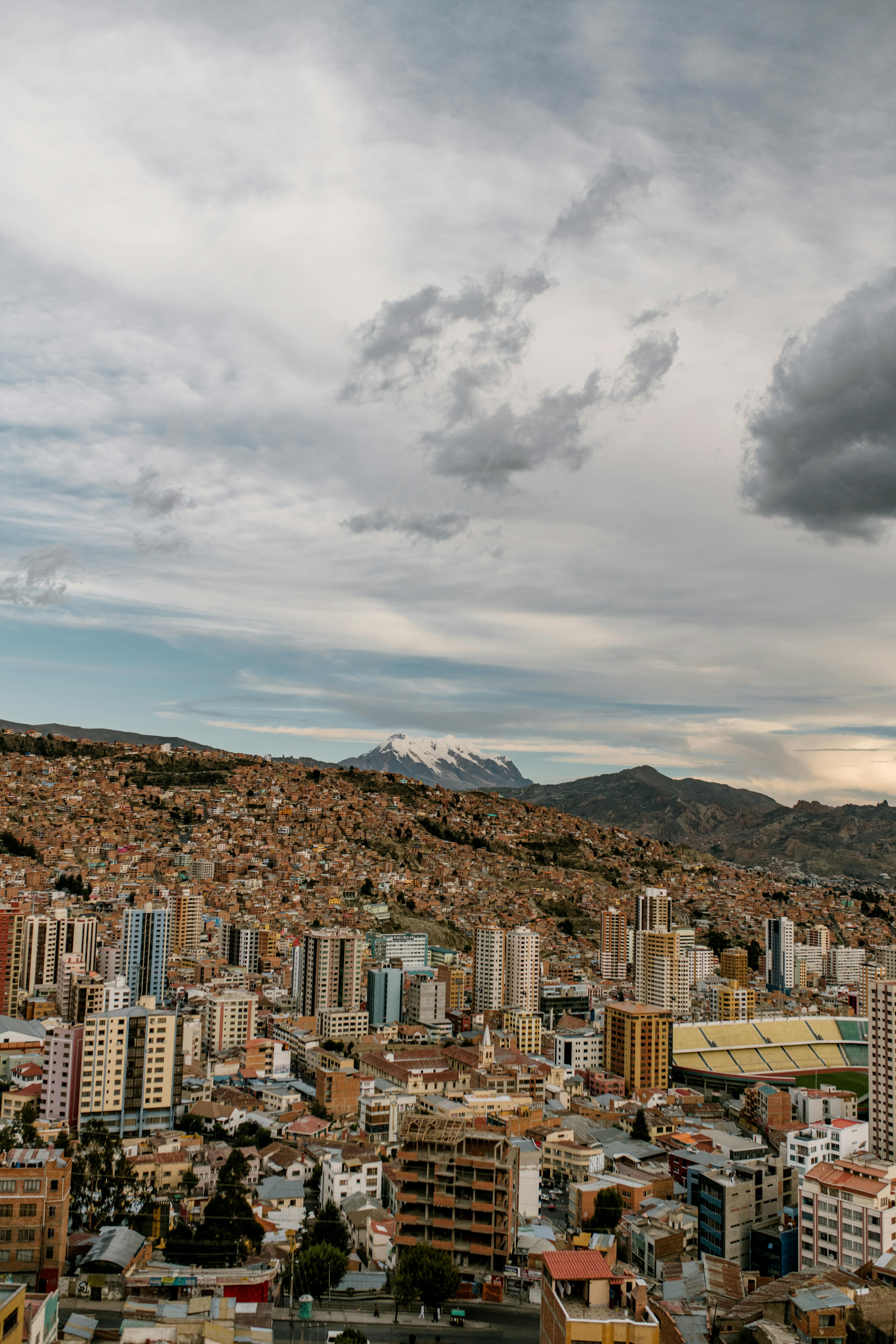 Odkryj oszałamiający widok z lotu ptaka na La Paz z tętniącym życiem pejzażem miejskim na tle majestatycznych gór pod zachmurzonym niebem.