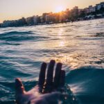 Brazylijska Chapada Diamantina: Raj dla miłośników trekkingu i przyrody Ręka wyciągająca rękę w kierunku złotego zachodu słońca nad plażą Vila Nova, chwytająca spokojny widok na ocean.