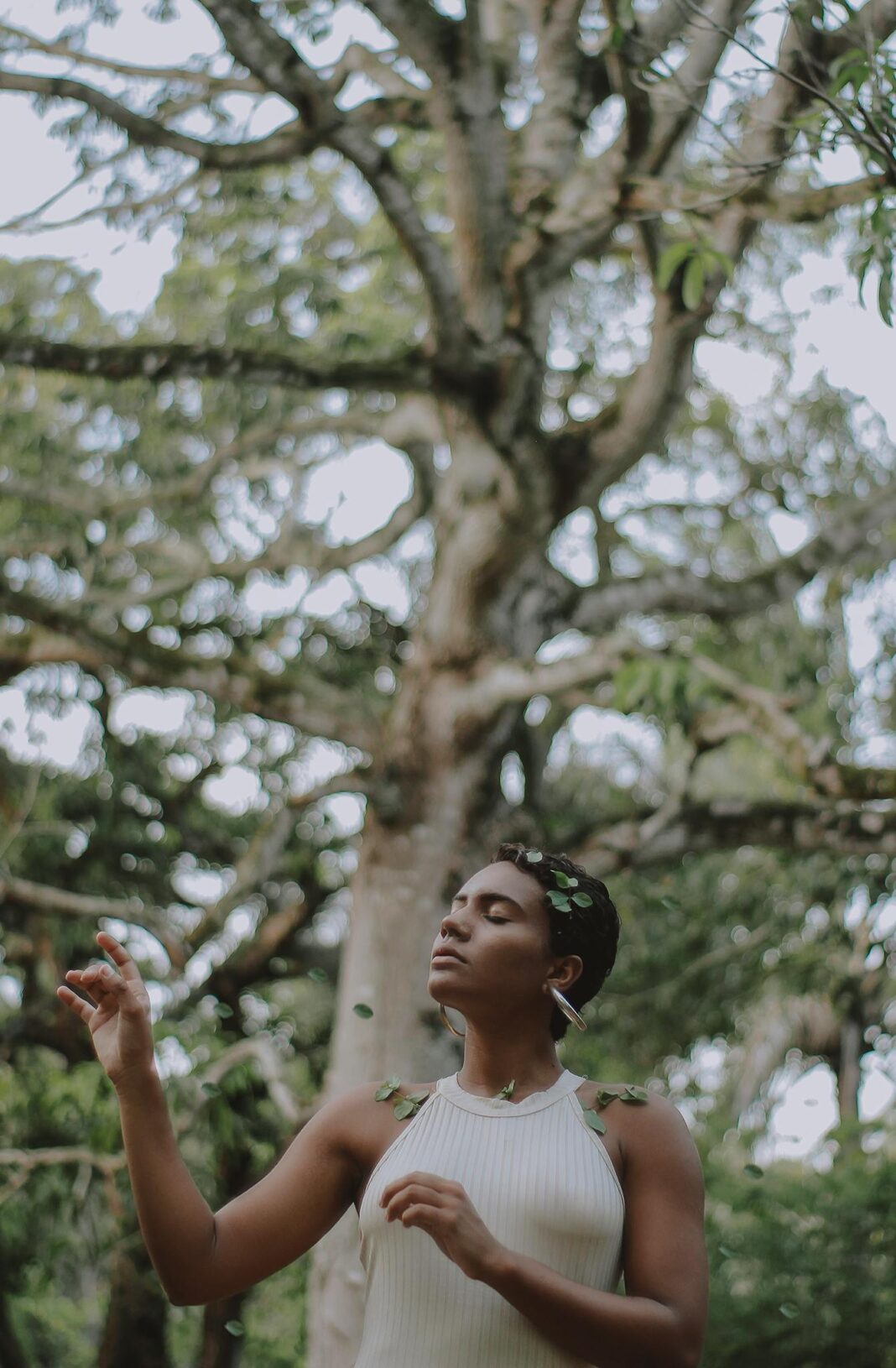 Spokojna kobieta pozuje na świeżym powietrzu z bujną zielenią drzew w tle, ucieleśniając spokój i połączenie z naturą.