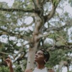 Spokojna kobieta pozuje na świeżym powietrzu z bujną zielenią drzew w tle, ucieleśniając spokój i połączenie z naturą.