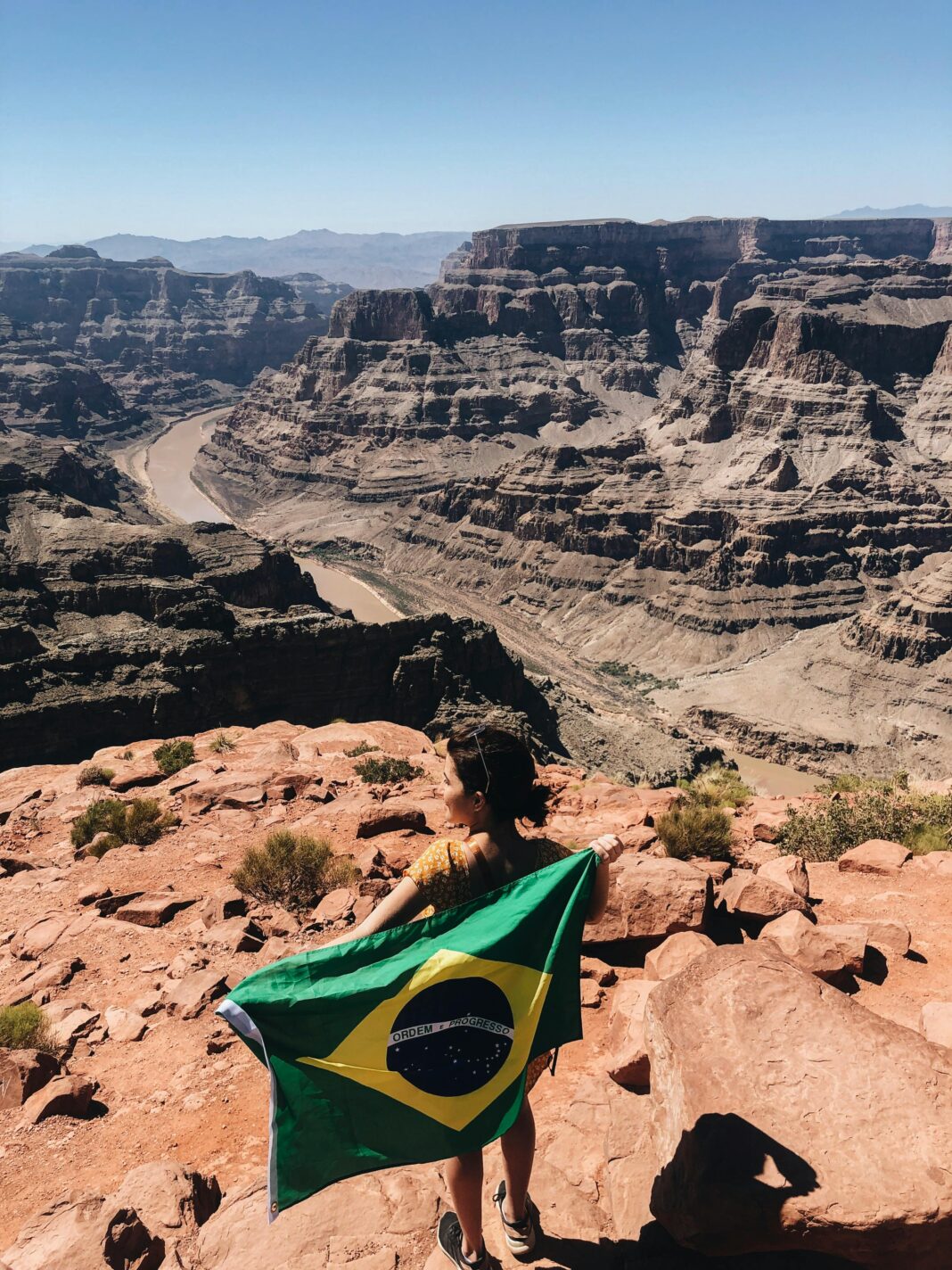 Kobieta trzyma brazylijską flagę na skraju wspaniałego Wielkiego Kanionu pod czystym niebem.