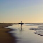 Sylwetka surfera o zachodzie słońca na plaży Campeche w Florianópolis w Brazylii, ukazująca spokojne piękno wybrzeża.