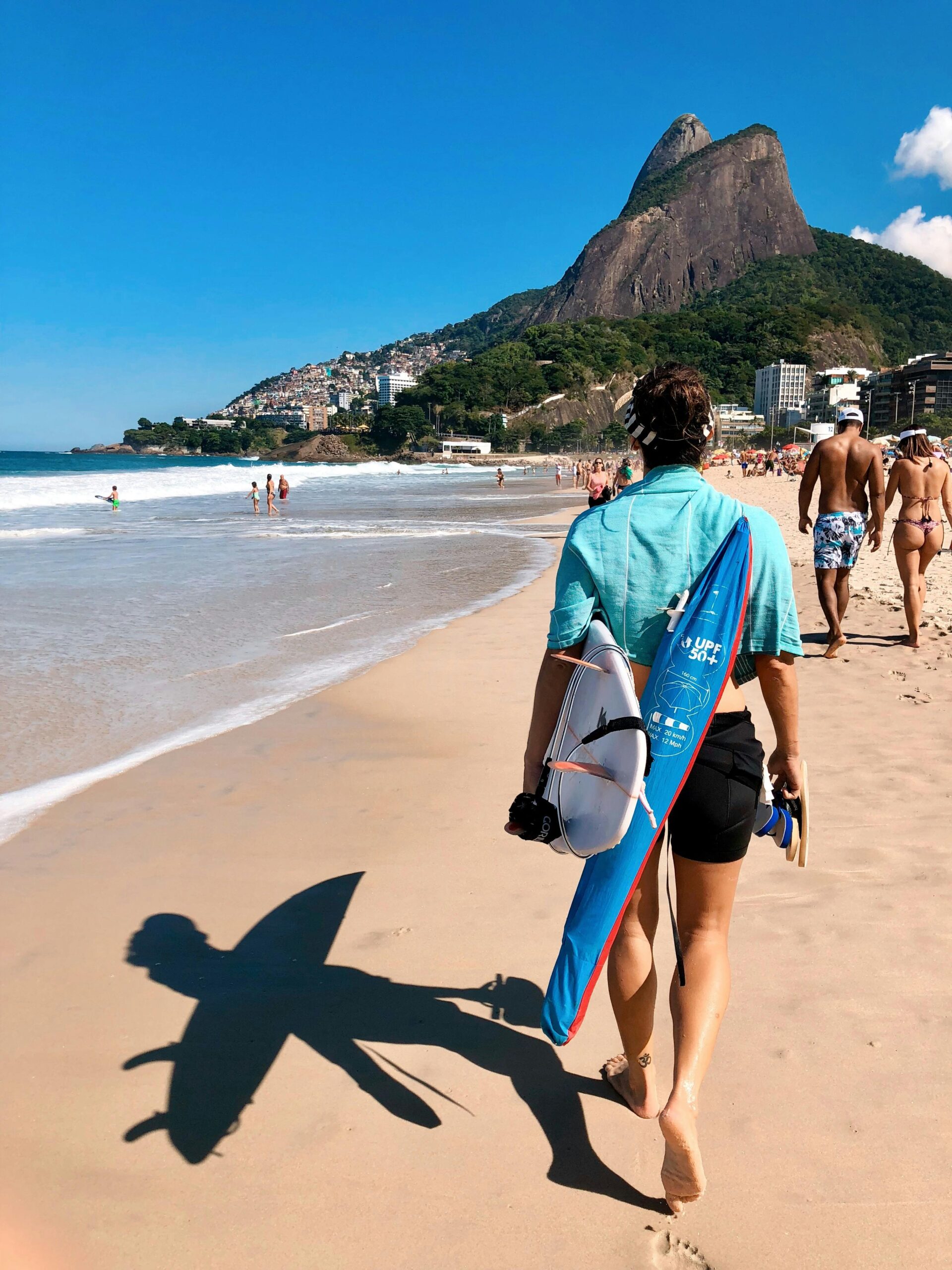 Surfer z deską spaceruje po plaży Ipanema w Rio de Janeiro, pod słonecznym niebem, na tle malowniczych gór.