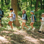By the help of a rope that is in hands. Group of children in the forest on a hike