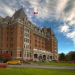 Historyczny hotel Empress w Wiktorii w Kanadzie pod tętniącym życiem błękitnym niebem z kolorowymi ogrodami i kanadyjską flagą.