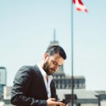 Kanada w zimie: Najlepsze miejsca na narty i snowboard Biznesmen stojący na zewnątrz i korzystający z telefonu z flagą Kanady w tle.