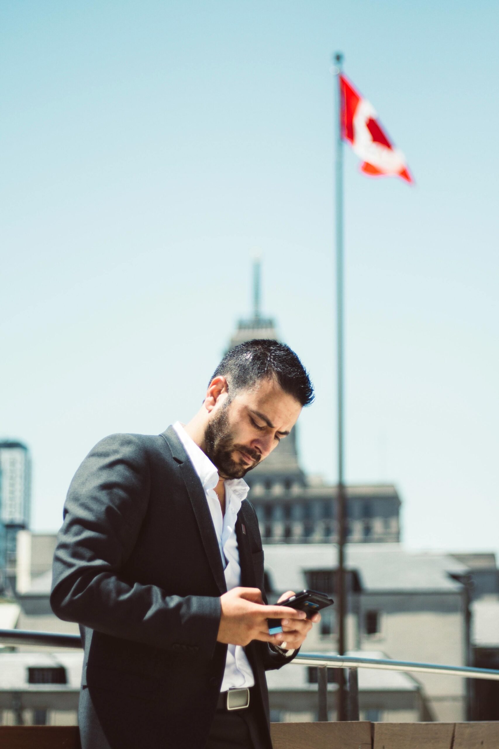 Biznesmen stojący na zewnątrz i korzystający z telefonu z flagą Kanady w tle.
