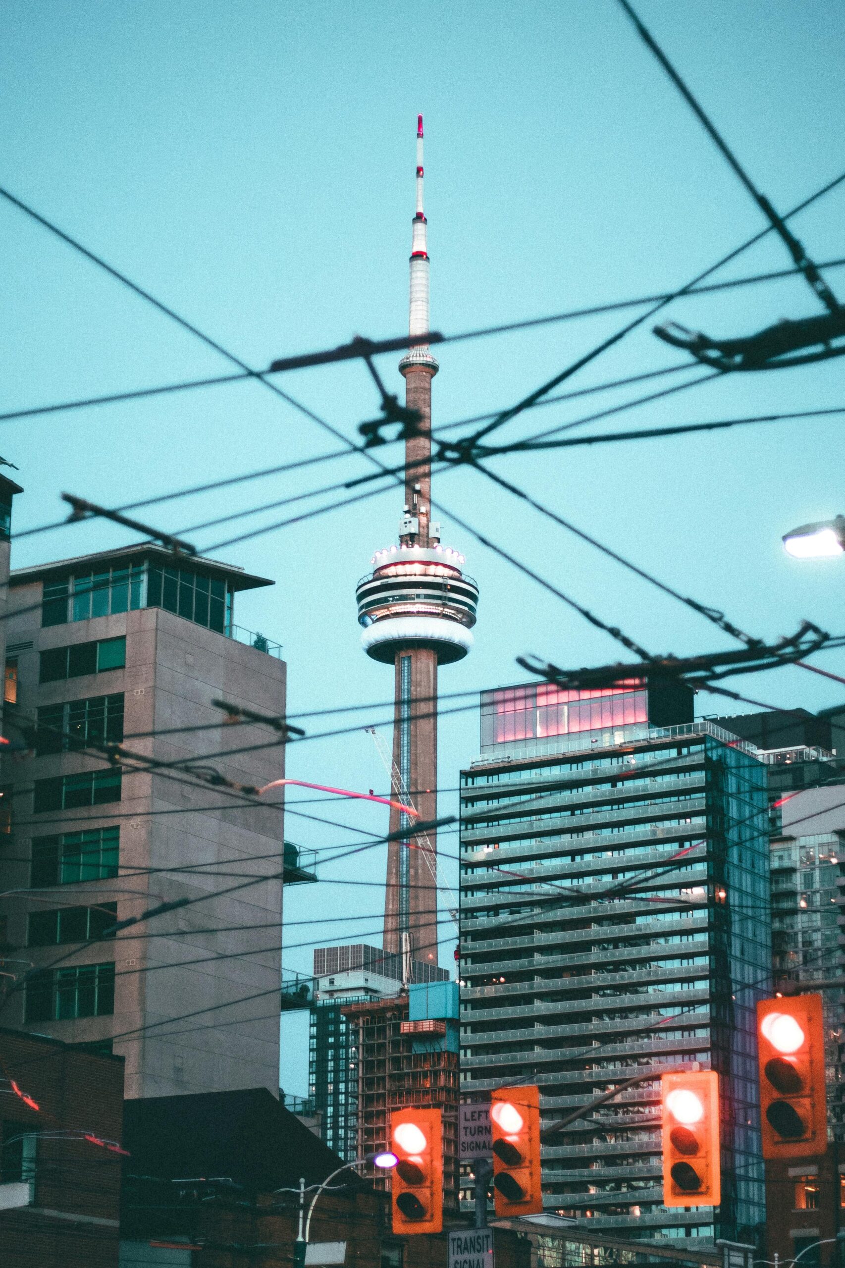 Charakterystyczny widok na wieżę CN Tower w Toronto otoczoną architekturą miejską i sygnalizacją świetlną.