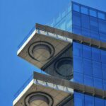 Zbliżenie nowoczesnego szklanego budynku z uderzającymi geometrycznymi elementami architektonicznymi na tle czystego, błękitnego nieba.