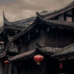 Zabytkowy chiński budynek z ozdobnymi dachami i czerwonymi latarniami pod zachmurzonym niebem.