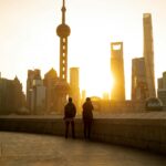 Sylwetki ludzi na tle oszałamiającej panoramy Szanghaju o zachodzie słońca, z charakterystycznymi drapaczami chmur.
