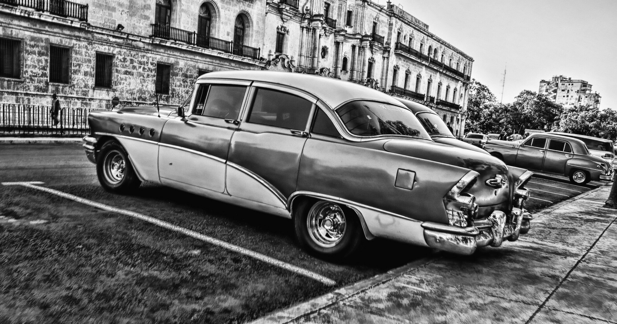 Czarno-białe zdjęcie klasycznego samochodu zaparkowanego w Hawanie na Kubie, przedstawiające styl i architekturę vintage.
