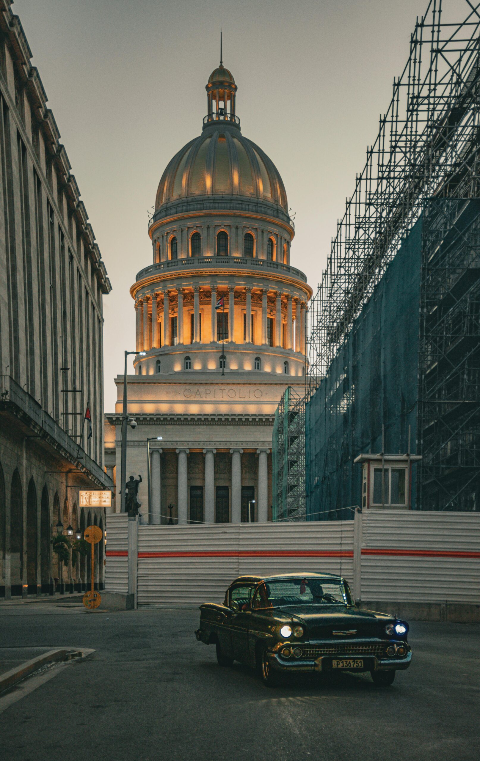 Klasyczny zabytkowy samochód przed El Capitolio w Hawanie o zmierzchu z rusztowaniami na ulicy.