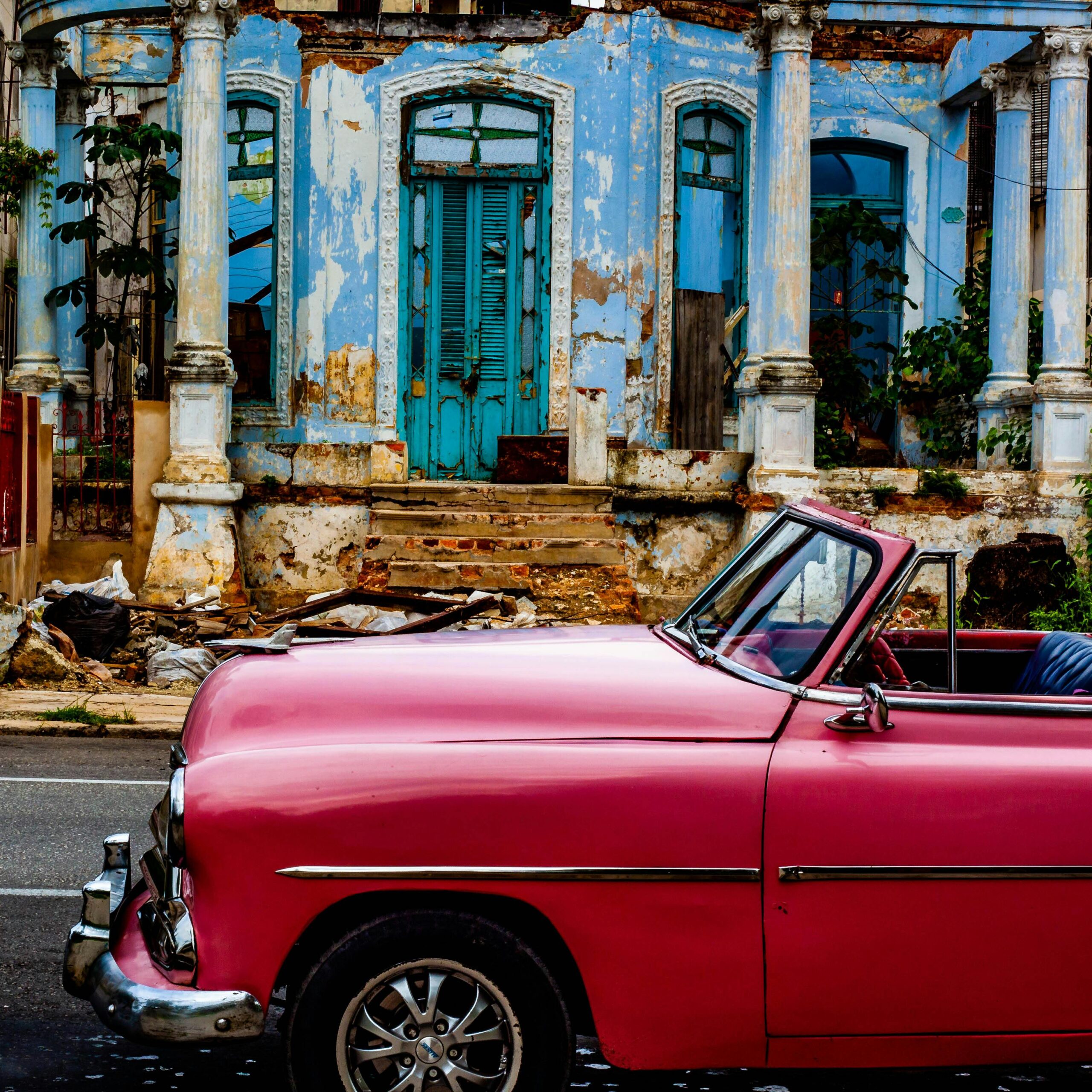 Klasyczny różowy samochód zaparkowany przy zniszczonym budynku w Hawanie, ukazujący nostalgiczny miejski urok.