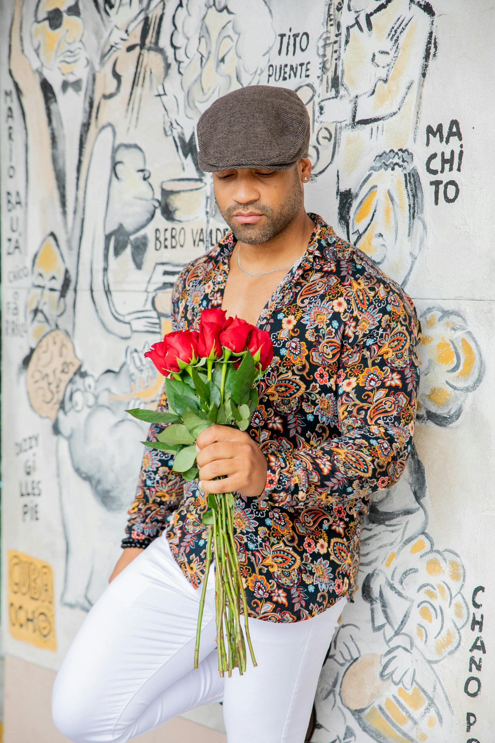 Stylowy mężczyzna trzymający róże na tle tętniącego życiem muralu w Hawanie na Kubie.