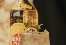 Tradycje i zwyczaje na Kubie – przewodnik podróżnika Zbliżenie orzeźwiającego koktajlu mojito z miętą i limonką przed butelką Havana Club.