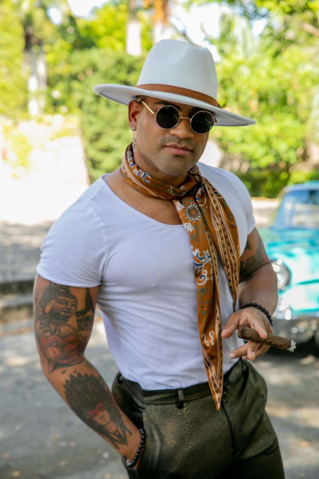 cuba Modny mężczyzna w kapeluszu i okularach przeciwsłonecznych stojący obok zabytkowego samochodu w pejzażu miejskim.